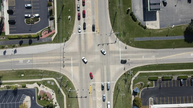 Static aerial establishing shot of intersection in the American suburbs. Traffic signal light, cars stopped at light, traffic drives on road, drone above cars.
