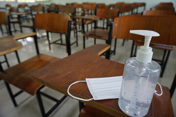 Medical face mask and alcohol hand wash gel for protecting anti-bacteria anti-virus and Coronavirus disease COVID-19 outbreak on wood lecture chairs in the empty classroom. Back to school concept.