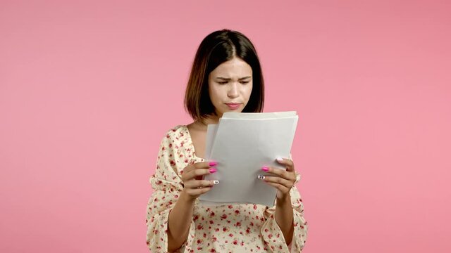 Distressed angry woman holding files papers, scatters them isolated on pink background. Pretty girl checks documents, utility bills.