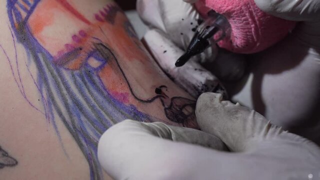 Tattooist making a tattoo of girl face on white skin, closeup view