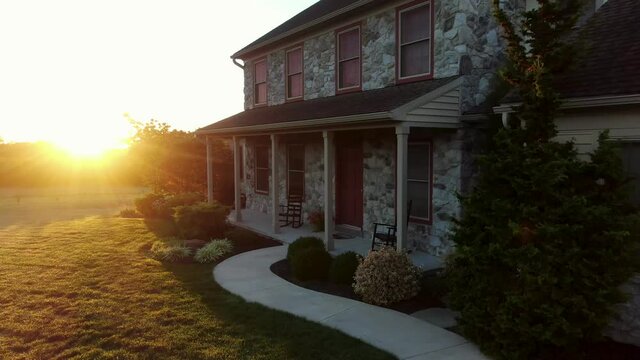 Rising aerial of front of traditional stone house. Curvy sidewalk leads to front door and porch of home. Morning sunrise in United States of America, USA.