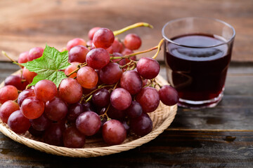 Fresh red grapes fruit in a basket and juice on wooden background