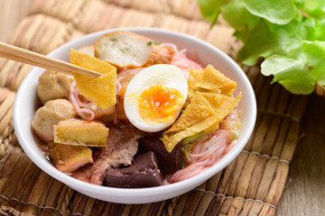 Thai food (Yen Ta Fo), Rice noodles soup with red sauce and fish tofu, pork ball and fried wonton eating by chopsticks