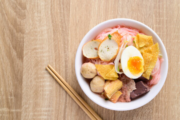 Thai food (Yen Ta Fo), Rice noodles soup with red sauce and fish tofu, pork ball and fried wonton in a bowl with chopsticks on wooden background, Top view