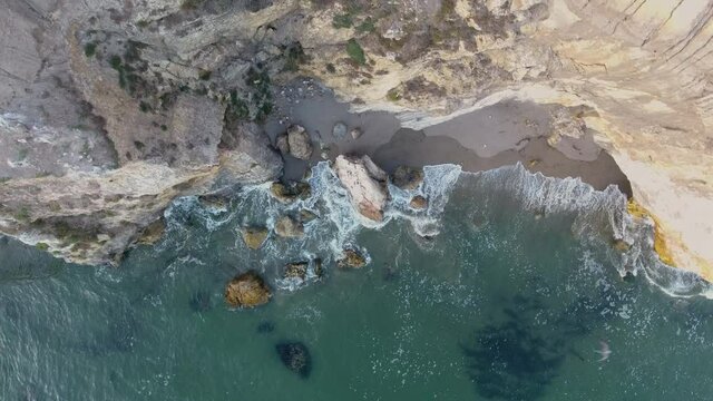 Aerial view of water with waves crashing on rocks and cliff shot in 4k high resolution