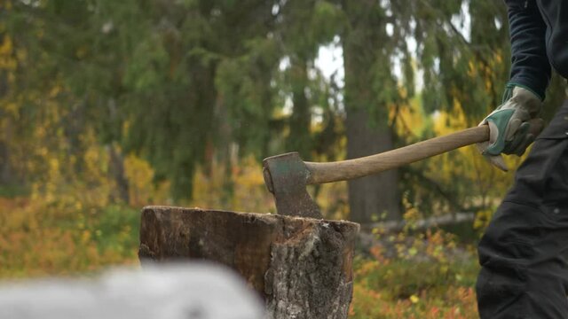 Man chopping fire wood with axe in the middle of a forest during the fall - Slide medium shot