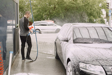 Man in a black sweater. Male washing a car. Guy spray a water.