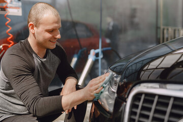 Man in a black sweater. Worker wipes a car. Male holding a rag in his hand.