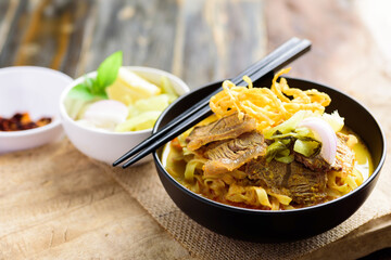 Northern Thai food (Khao Soi), Spicy curry noodles soup with beef in a bowl eating with crispy deep-fried egg noodles, pickled mustard, shallots, lime and ground chillies fried in oil