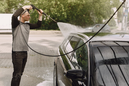 Man in a black sweater. Male washing a car. Guy spray a water.