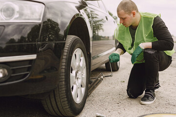 Worker changes a broken wheel of a car. The driver should replace the old wheel with a spare. Man changing wheel after a car breakdown.