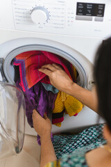 Woman doing laundry , hand loading soiled clothes into front load automatic washing machine ,  new technology electronic device different programs to wash cotton , wool in temperature Kerala India.