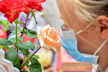 A girl in a protective mask holds a bouquet of flowers and sniffs roses, quarantined for the...