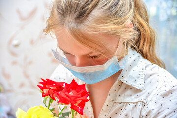 A girl in a protective mask holds a bouquet of flowers and sniffs roses, quarantined for the...
