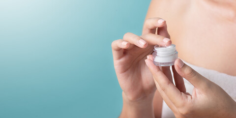 Close Up hand holding cosmetic cream jar with cosmetic product on light blue background.