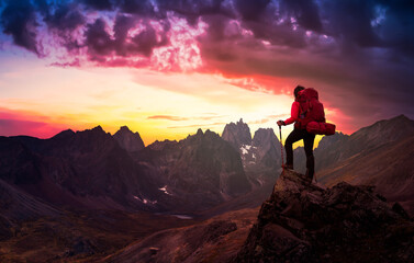 Woman Standing on Rocks looking at Scenic Mountain Peaks and Valley, Fall in Canadian Nature. Dramatic Twilight Sky Adventure Composite. Bacground Landscape, Tombstone Territorial Park, Yukon, Canada.