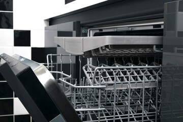 close-up of a dishwasher without dishes, on the background of black and white kitchen tiles