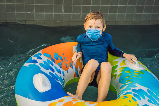 Little boy swimming with rubber ring at the leisure center wearing a medical mask during COVID-19 coronavirus