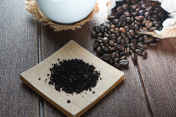 A cup of coffee, coffee beans and coffee powder on a wooden surface