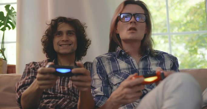 Excited men friends enjoying video games sitting on couch at home