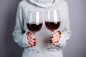 A woman in a white sweater is holding two glasses of red wine. Close up