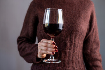 A woman in a brown sweater is holding a glass of red wine in her hand. Close up