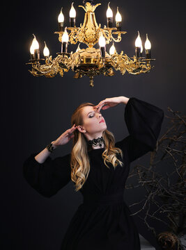 Beautiful blonde young woman in black dress in the light of chandelier