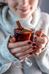 A woman in a white warm sweater is holding a transparent glass cup of mulled wine in her hand. Concept of a cozy atmosphere and a traditional winter drink