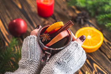 Obraz na płótnie Canvas Women's hands in a white warm sweater are holding a glass cup with mulled wine. Concept of a cozy atmosphere and a nice winter mood with a aromatic hot traditional drink