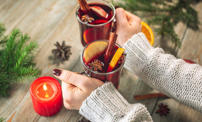 Women's hands in a white warm sweater are holding a glass cup with mulled wine. Concept of a cozy...