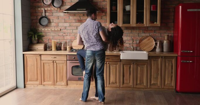 Full-length happy couple hold hands circling whirling while dancing barefoot in kitchen enjoy active weekend, modern kitchen interior with wooden floor underfloor heating system, romantic date concept
