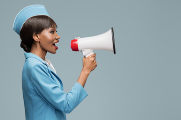 Cheerful young african stewardess shouts into the loudspeaker. Blue background.