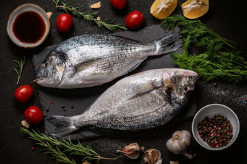 Fresh fish dorado with ingredients for cooking on dark background