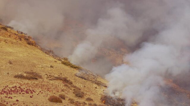 Smoke rising into the air from grassfire burning on mountain in Utah as it works up the hillside.