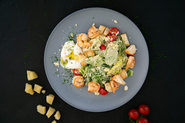 Caesar salad with shrimp and soft-boiled egg on a gray plate and a black background