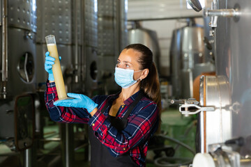 Female winemaker in protective mask analyze the white wine in a beaker