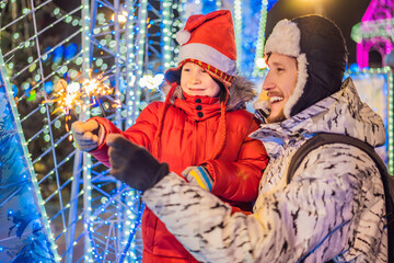 Little boy and his father with sparklers near giant fir tree and Christmas illumination on Christmas market. Xmas holidays on fair