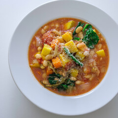 Ribollita or minestrone soup with beans, butternut squash, kale, bay leaf, and parmesan cheese. Top view on white background.
