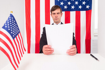 An American reads documents. A man in a business suit next to the flags of the United States. Moving to America. Immigration to the United States of America. Business in USA.