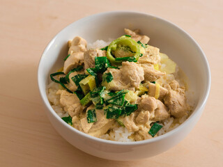 Curry chicken with leeks over rice served in a white bowl