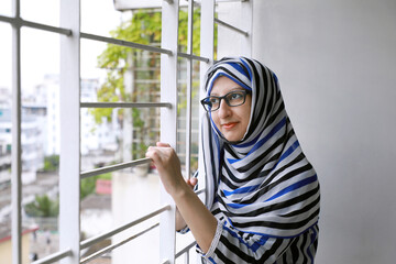 Young Bengali Muslim woman wearing hijab (head scarf) standing on balcony