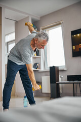 Energetic aged man doing physical exercises at home