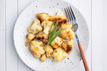 Fried cauliflower florets in batter on a white plate. White wooden background.