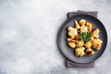 Fried cauliflower florets in batter on a black plate. Grey concrete background. Copy space.