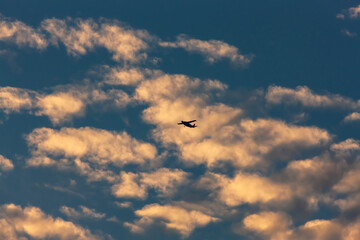 Blue sky with puffs of clouds and a small silhouette of an airplane