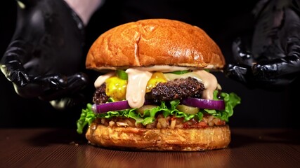 Craft burger is cooking on black background. Consist: red sauce salsa, lettuce, red onion, pickle,...