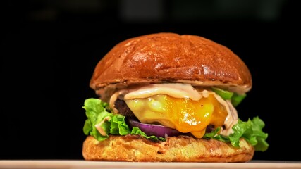 Craft burger is cooking on black background. Consist: red sauce salsa, lettuce, red onion, pickle, cheese, chilli green pepper, air bun and marbled meat beef. Not made ideal. Loving hand made.