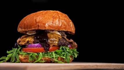 Craft burger is cooking on black background. Consist: sauce, arugula, tomato, red onion, bacon, red...