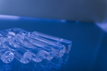 Glass medical ampoule vial for injection. Medicine is liquid sodium chloride with of aqueous solution in ampulla. Close up. Bottles ampule multicolor on background color and water. Human plasma.