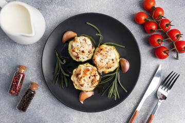 Baked stuffed zucchini columns with minced chicken and vegetables on a plate. Grey concrete background. copy space